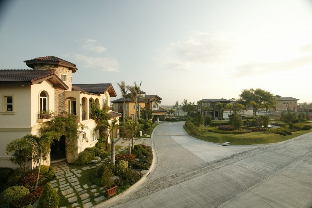 Warm summer day in Italian inspired themed community of yellows and oranges, and cobblestone designed roads and old classic lamp posts, and a lush green courtyard of small hedges with a water fountain in the center | Luxury Homes by Brittany Corporation