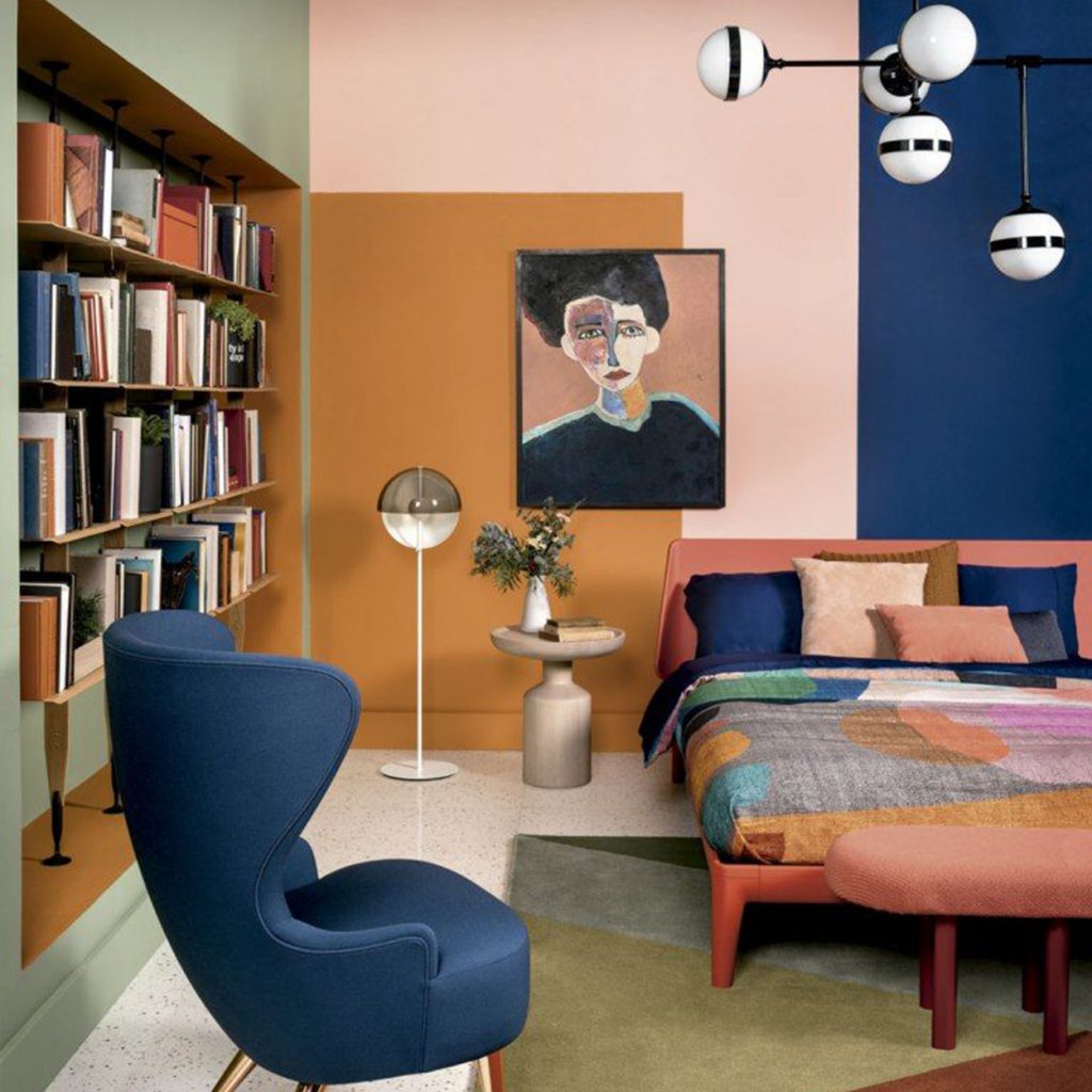 70s mod style room with bookshelf on the left side a blue chair and colorful bed with an abstract painting with a weird lighting fixture in a luxury mansion | luxury homes by brittany corporation