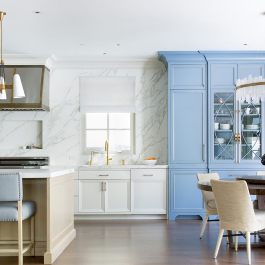 kitchen with blue, marble, and white walls with a center island and bar stool on the left side and a circle table with a chandelier above in a luxury mansion | luxury homes by brittany corporation