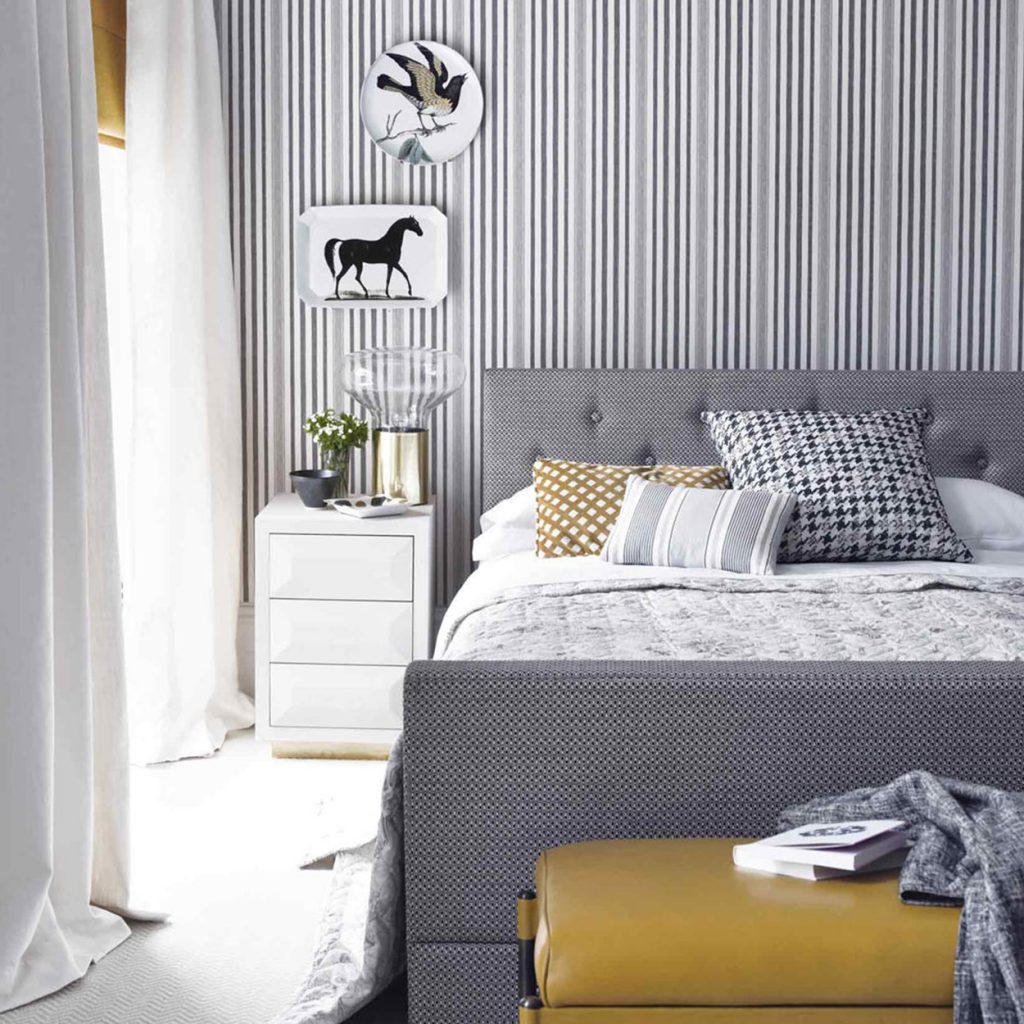 pinstripe wallpaper with decorative plates with a bird and horse design white on the wall white curtains and end table gray bed in a luxury mansion and yellow ottoman | luxury homes by brittany corporation