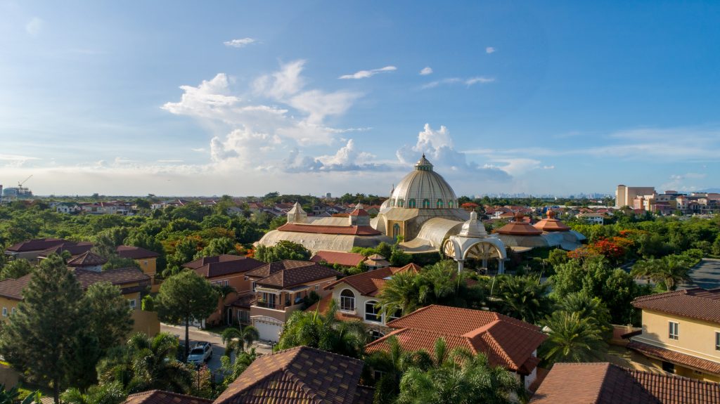 Panoramic view of warm Italian houses surrounded by tall palm trees and pine trees, and rising above them all is a classic European orthodox style church.