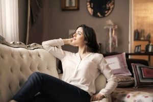 A young caucasian woman with brown hair relaxing on her Victorian-inspired couch in the living room of her luxury house | Luxury Homes by Brittany Corporation