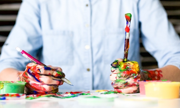 Man holding messy brushes with paint all over his hands and the table | Luxury Homes by Brittany Corporation