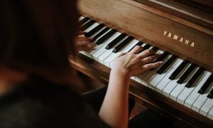 Over the shoulder picture of a woman practicing playing the piano on her Yamaha wooden grand piano | Luxury Homes by Brittany Corporation