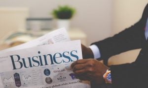 An African-American man in a black suit with a blue watch reading the Business section of the newspaper | Luxury Homes by Brittany Corporation