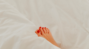 A light skinned foot with red nail polish resting on the comforter and beddings in her luxury home | Luxury homes by Brittany