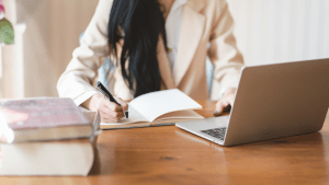 body of an Asian woman with long hair, taking down notes in front of her laptop, inside her home office