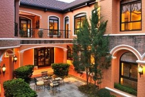 Inside view of the courtyard of an orange mansion, with trees, bushes, and a lanai breakfast area; with the second floor indoor veranda overlooking the courtyard | Vista Alabang | Portofino | Luxury Homes by Brittany Corporation