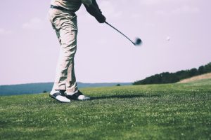 Person playing golf in a golf course with vibrant greenery - Luxury Homes by Brittany Corporationn