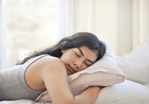 Sleeping Southeast Asian woman in her teens or early twenties, comfortably staying at home and in a bed of white pillows and duvet, in the daytime | Luxury Homes by Brittany Corporation