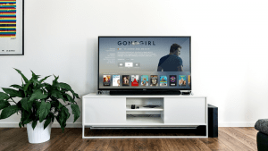 Flat screen TV previewing Gone Girl movie on a white desk table, next to a potted leafy green plant, in a modern minimalist white living room with dark wooden flooring | Luxury Homes by Brittany Corporation