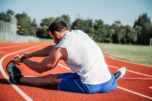 Western brunette man with facial hair and a muscular body, stretching his leg on the floor in a running track | Luxury Homes by Brittany Corporation