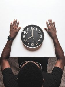 A man staring at a clock on his table to monitor his time while working remotely | Luxury Homes by Brittany Corporation