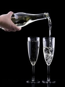 Two glasses of sparkling wine being poured by a caucasian male on a black background | Luxury Homes by Brittany Corporation