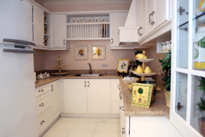 Small traditional white kitchen with fruits on display, potted plants, framed flower portraits, and ceramic mugs for show in wooden wall cabinets | Luxury Homes by Brittany Corporation