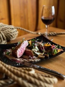 A platter of medium rare rib-eye steak with various vegetables along with a glass of red | Luxury Homes by Brittany Corporation