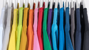 Rainbow colored closet with colorful shirts on grey hangers in a white cabinet | Luxury Homes by Brittany Corporation