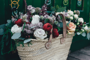 A woven basket bag with leather handles, filled with dainty and colorful roses, vines, leaves, and berries | Luxury Homes by Brittany Corporation