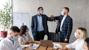 Two male bosses elbow bump each other as the rest of the team look up to them in an office meeting | Luxury Homes by Brittany Corporation