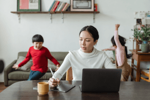 Asian mother working from home while her two children are playing in the living room of their luxury home | Brittany Corporation