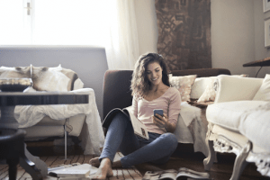 Brown haired Scandinavian woman looking at magazines and her phone in comfortable clothes, sitting on the living room floor during the rainy season