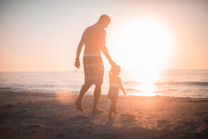 Father and son walking along the shore of a beach during sunset | Brittany Corporation
