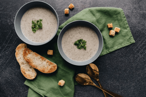 Flatlay of bowls of cream of mushroom soup, bread, croutons, and golden spoons are perfect for the rainy season