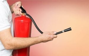 Man holding fire extinguisher which is one of the most essential items with a background with red pink and orange gradient | Luxury Homes by Brittany Corporation