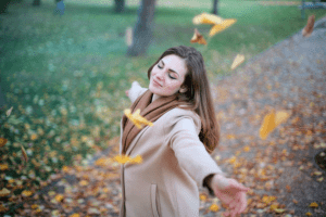 Woman pamper herself while twirling around in a nature park with falling leaves near her luxury home for sale - Brittany Corporation