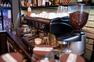 Workplace of contemporary barista with coffee machine, clean cups and glasses and bottles with alcohol on shelf above | Luxury Homes by Brittany Corporation