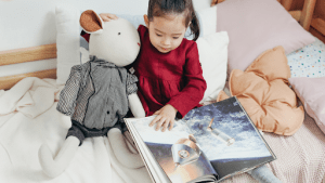 Young child playing with her sheep plush toy while reading a childrens book about space in her luxury home | Brittany Corporation