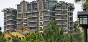 Blue-green condominium hotel or condotel with brown and yellow accents sit atop a lush pine tree forest, under a cold cool breezy foggy sky, with a classic black lamp post in focus