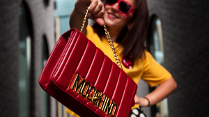 Red Moschino designer bags held by brunette with red sunglasses on | Luxury Homes by Brittany Corporation