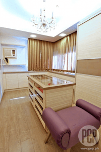 Walk in closet with light-colored wooden cabinets and wooden floors and classic chandelier.