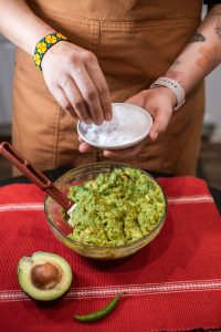 Woman making guacamole adding salt and chipotle pepper luxury home kitchen with arm tattoos | Luxury Homes by Brittany Corporation