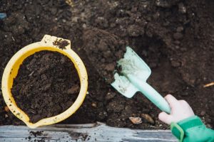 Young child digging soil practicing composting for healthy plants | Luxury Homes by Brittany Corporation