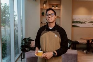 Man with brown apron holds barista-style mug at home | Luxury Homes by Brittany Corporation