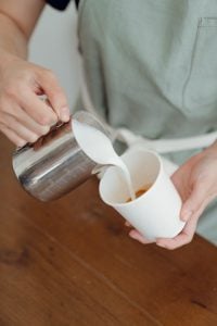 Barista pouring milk into a cup of espresso to create latte at his luxury home | Luxury homes by Brittany corporation