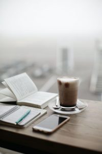 A table in a luxury condominium with a book, notebook, pen, phone, and barista-style mug | Luxury Homes by Brittany Corporation