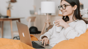 western girl with glasses comfortable in her luxury home living room while sipping coffee and searching for a lot only property on her laptop | luxury lifestyle and homes at brittany corporation