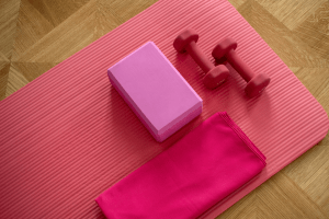 Pink indoor gym workout essential equipment including barbels, yoga block, yoga mat, and towel.