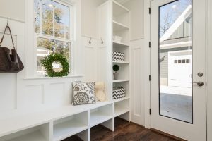 A landscape photo of a clean and spacious mudroom with white paintwork, wooden floor and cubbies, and a clear, glass door. | luxury homes by brittany corporation