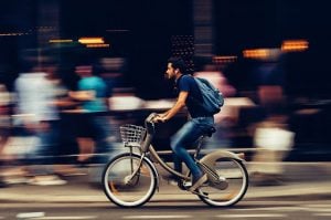 South Asian Man riding a bike on his way to his luxury home on a busy street with blurred people behind him | luxury homes by brittany corporation 