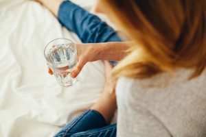 person holding a glass of water wearing denim pants and blonde hair about to drink water for her heart health in her luxury bedroom bed luxury homes by brittany corporation | Luxury Homes by brittany corporation