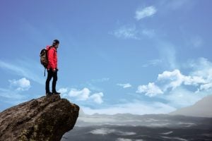 Mountain hiker in red jacket stands by the edge of a cliff | luxury homes by brittany corporation