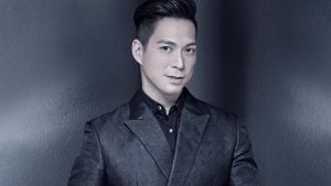 Francis Libiran in a geometric black suit staring at the camera with metallic gray background luxury house and lot