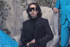 Michael Cinco Filipino fashion designer in black coat sitting on white chair in a luxury home with distress wall and ivy crawling | Luxury Homes by brittany Corporation