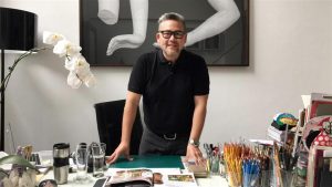 Rajo Laurel in black polo shirt in luxury home table with clutter man wearing glasses with expensive painting behind him | Luxury Homes by Brittany Corporation