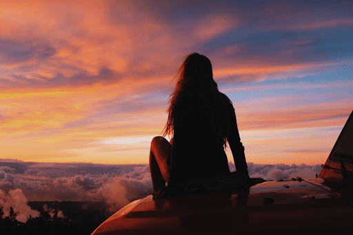 Woman watching the view of the golden hour from the hood of her car | Luxury Homes by Brittany Corporation