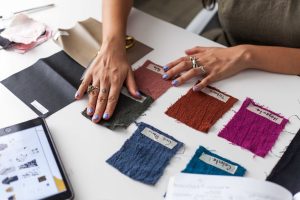 filipino fashion designer woman with blue nail polish compares two pieces of cloth on a white table inside a luxury home | Luxury Homes by Brittany Corporation